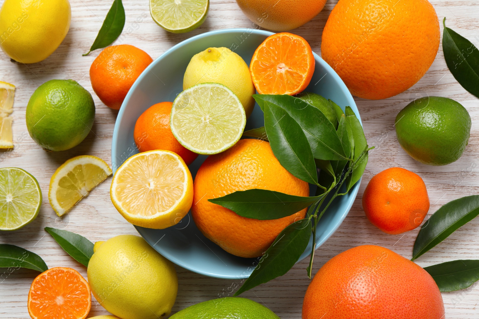 Photo of Different ripe citrus fruits with green leaves on white wooden table, flat lay