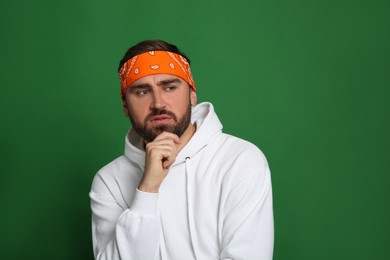 Fashionable young man in stylish outfit with bandana on green background, space for text