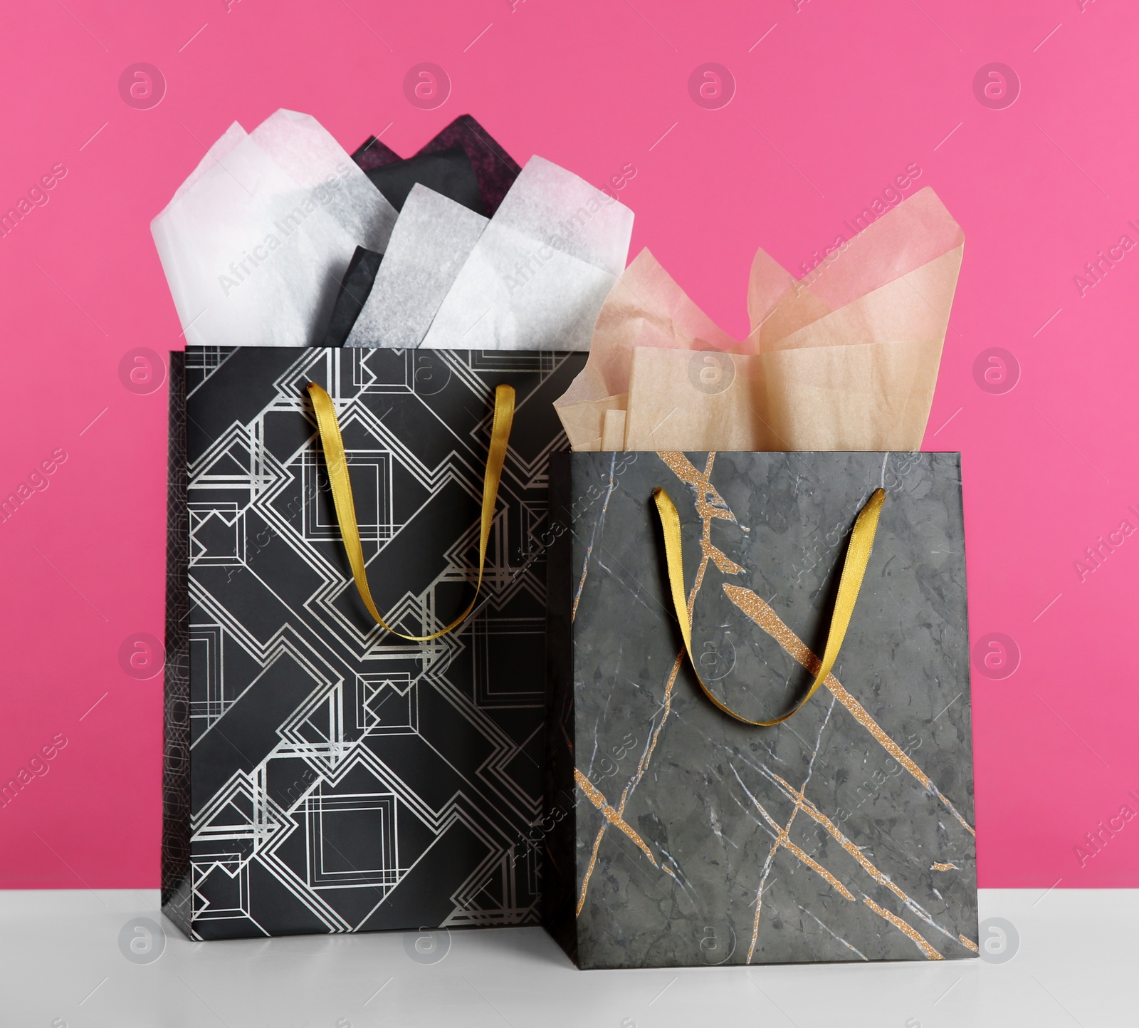 Photo of Gift bags with paper on white table against pink background