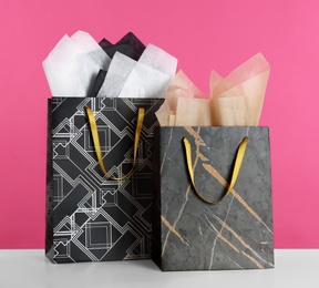 Photo of Gift bags with paper on white table against pink background