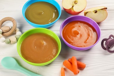 Photo of Baby food. Different purees in bowls, fresh ingredients, toy and soother on white wooden table