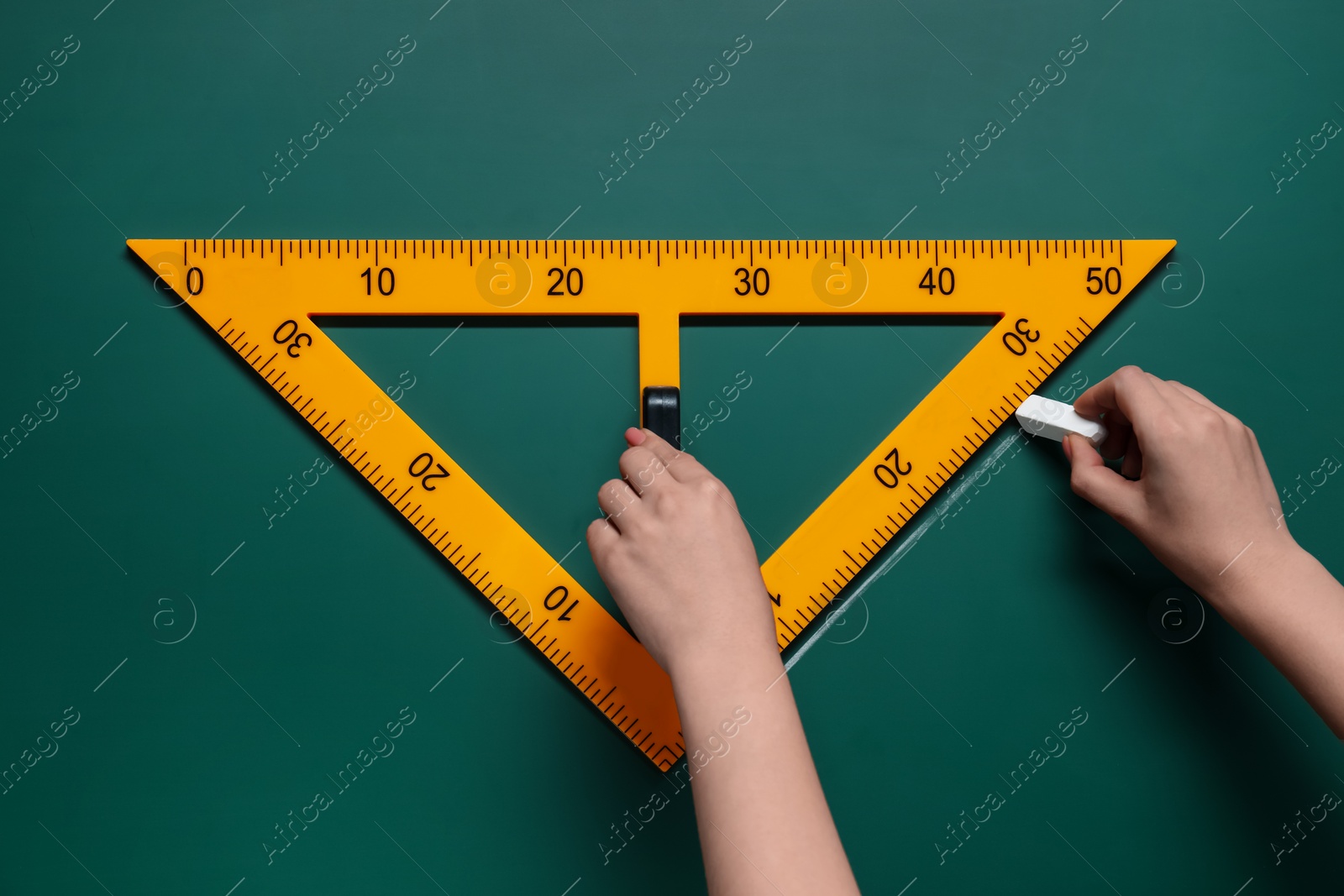 Photo of Woman drawing with chalk and triangle ruler on green board, closeup