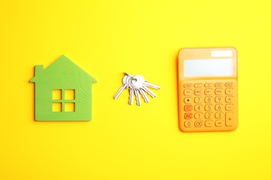 House figure with calculator and keys on yellow background, flat lay. Real estate agent service