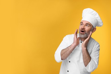 Photo of Surprised chef in uniform on orange background, space for text