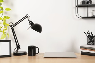 Cozy workspace with laptop, lamp and stationery on wooden desk at home