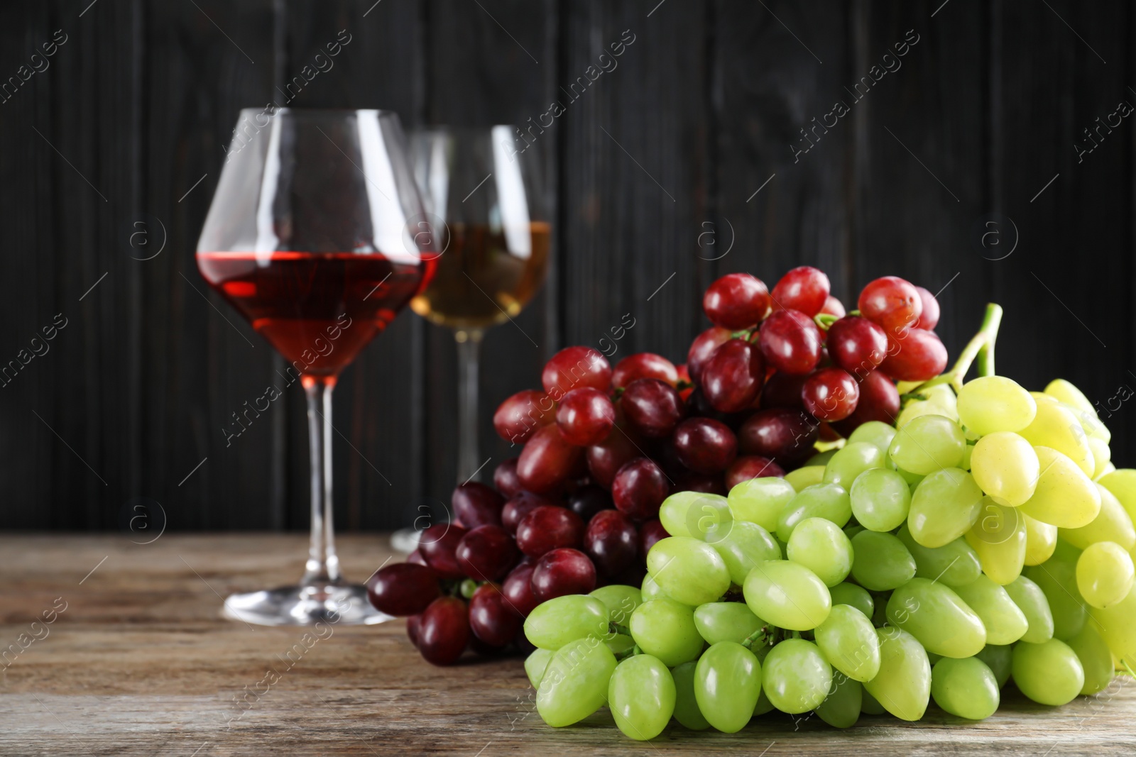 Photo of Fresh ripe juicy grapes and wine on wooden table against dark background