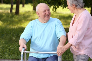 Photo of Elderly woman helping her husband with walking frame outdoors