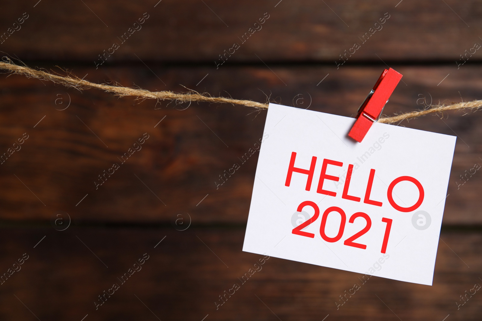 Image of Paper note with phrase Hello 2021 hanging on twine against wooden background, space for text