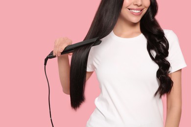 Photo of Happy woman using hair iron on pink background, closeup. Space for text