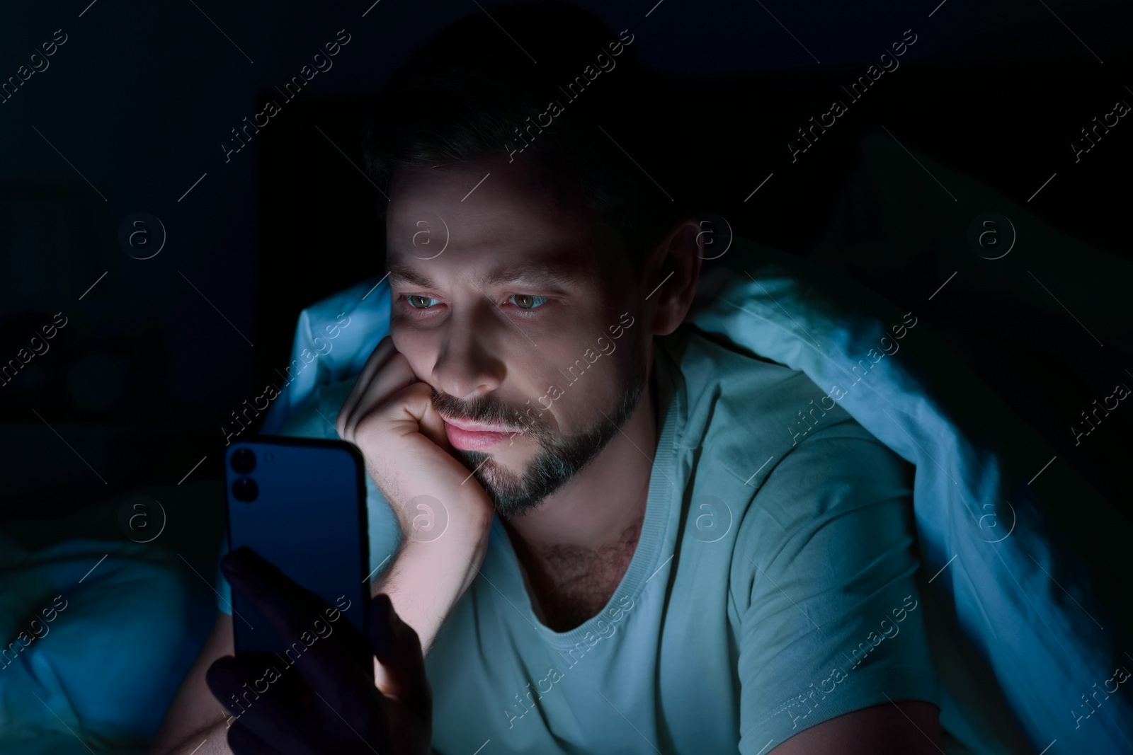 Photo of Man using smartphone in bed at night. Internet addiction