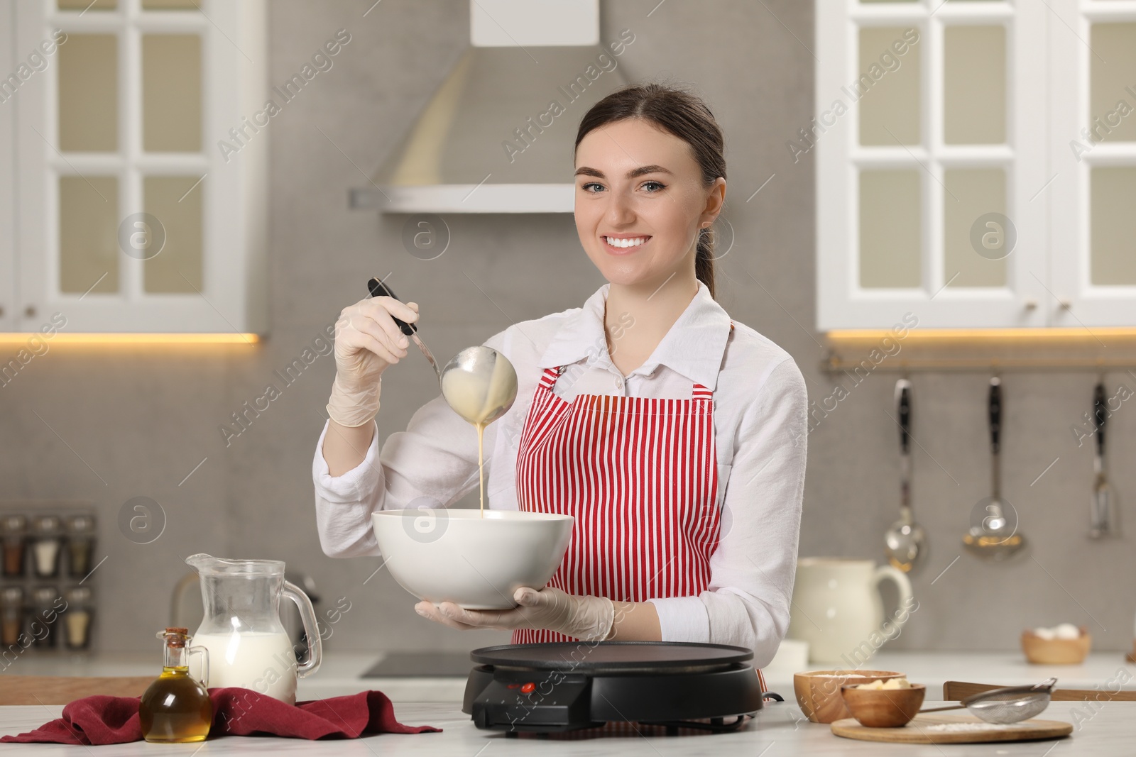 Photo of Young woman cooking delicious crepes in kitchen