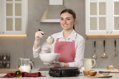 Young woman cooking delicious crepes in kitchen