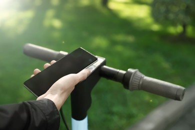 Photo of Man using smartphone to pay and unblock rental electric scooter outdoors, closeup