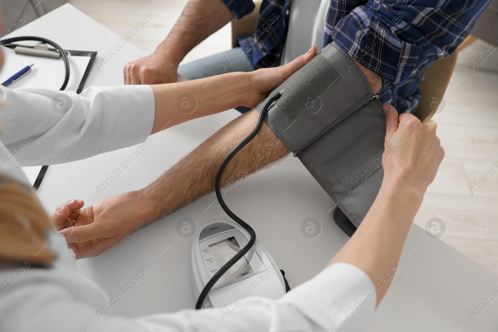 Photo of Doctor measuring blood pressure of man at table indoors, closeup