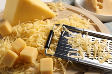 Photo of Grated, whole pieces of cheese and grater on table, closeup