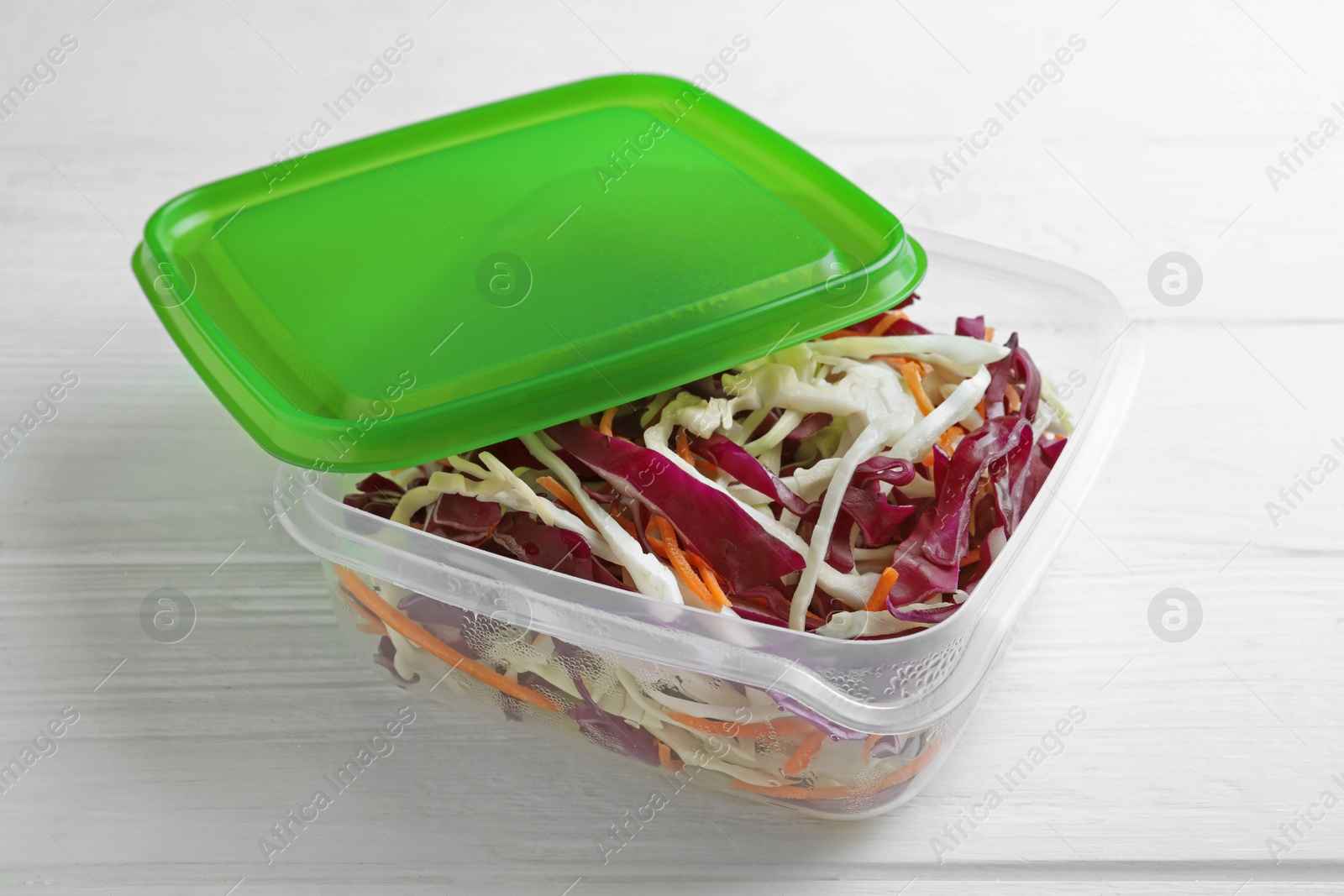 Photo of Fresh cabbage salad with shredded carrot in plastic container on white wooden table