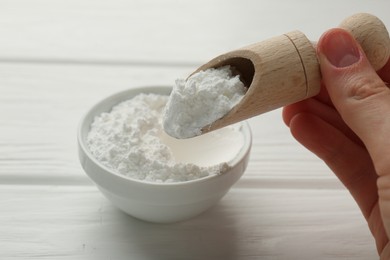 Photo of Woman taking baking powder with scoop from bowl at white wooden table, closeup