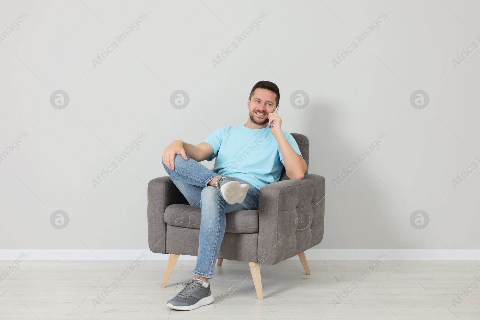 Photo of Happy man sitting in armchair and talking on smartphone indoors