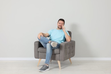 Happy man sitting in armchair and talking on smartphone indoors