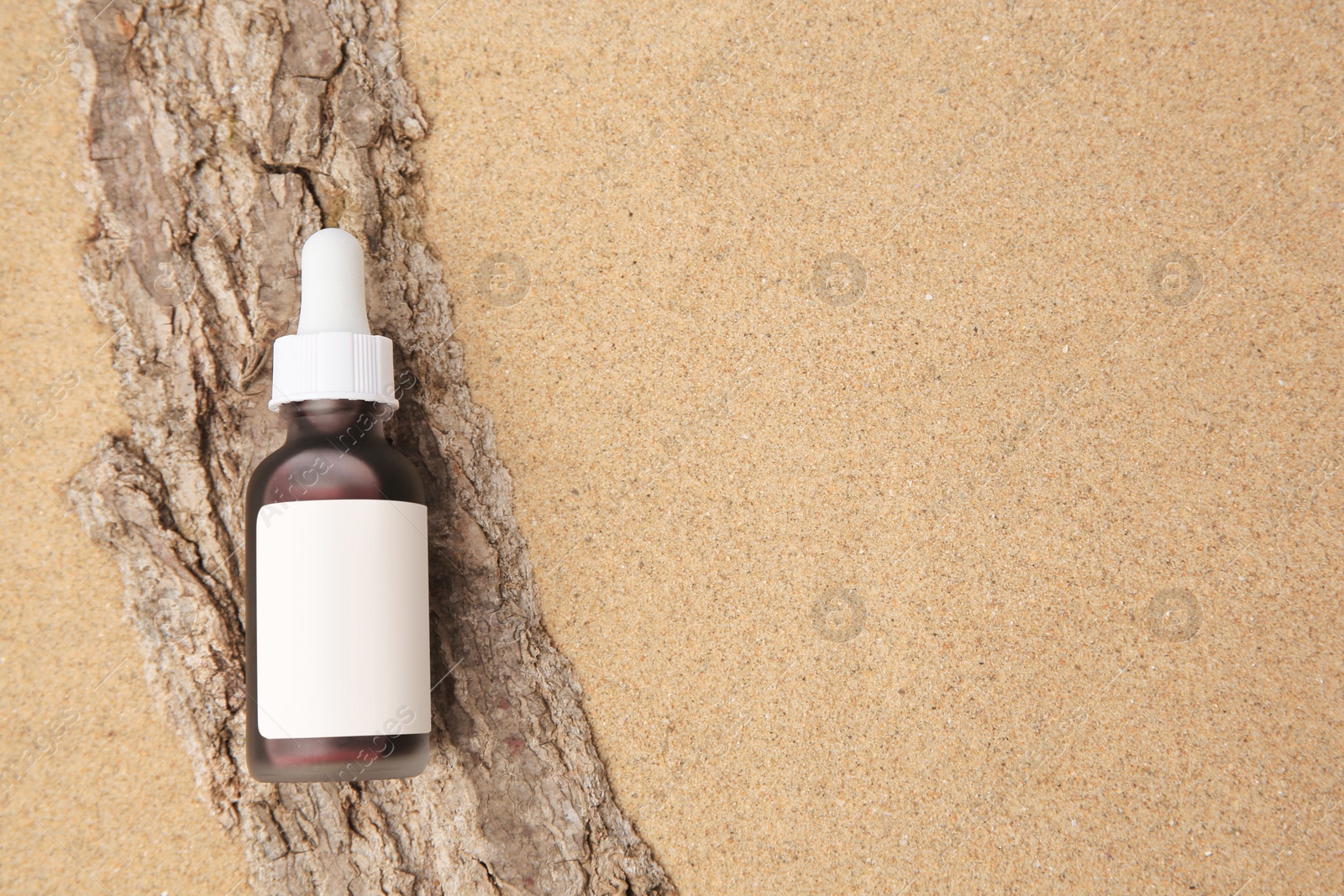 Photo of Bottle with serum and bark on sand, top view with space for text. Cosmetic product