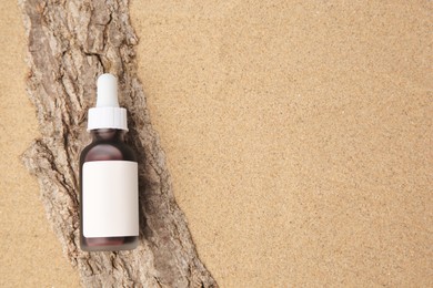 Bottle with serum and bark on sand, top view with space for text. Cosmetic product