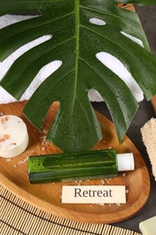 Card with word Retreat, different spa products and green palm leaf on table, above view