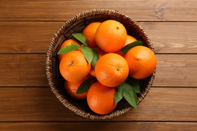 Photo of Delicious ripe oranges in wicker bowl on wooden table, top view