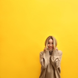 Beautiful young woman wearing knitted sweater on yellow background. Space for text