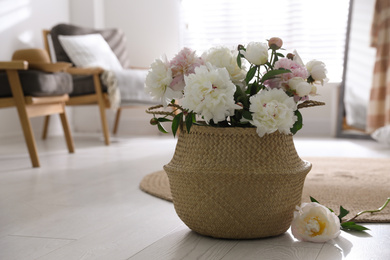 Photo of Bouquet of beautiful peony flowers in basket on floor. Space for text