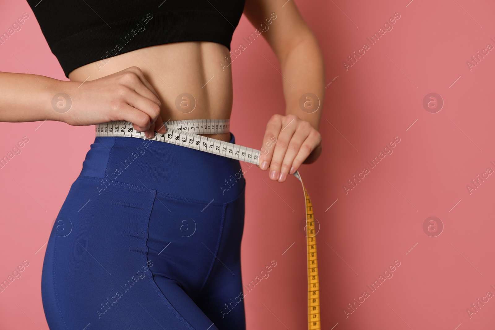 Photo of Woman in sportswear measuring waist with tape on pink background, closeup. Space for text