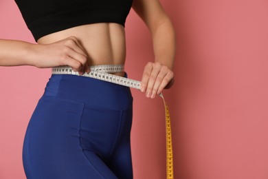 Photo of Woman in sportswear measuring waist with tape on pink background, closeup. Space for text