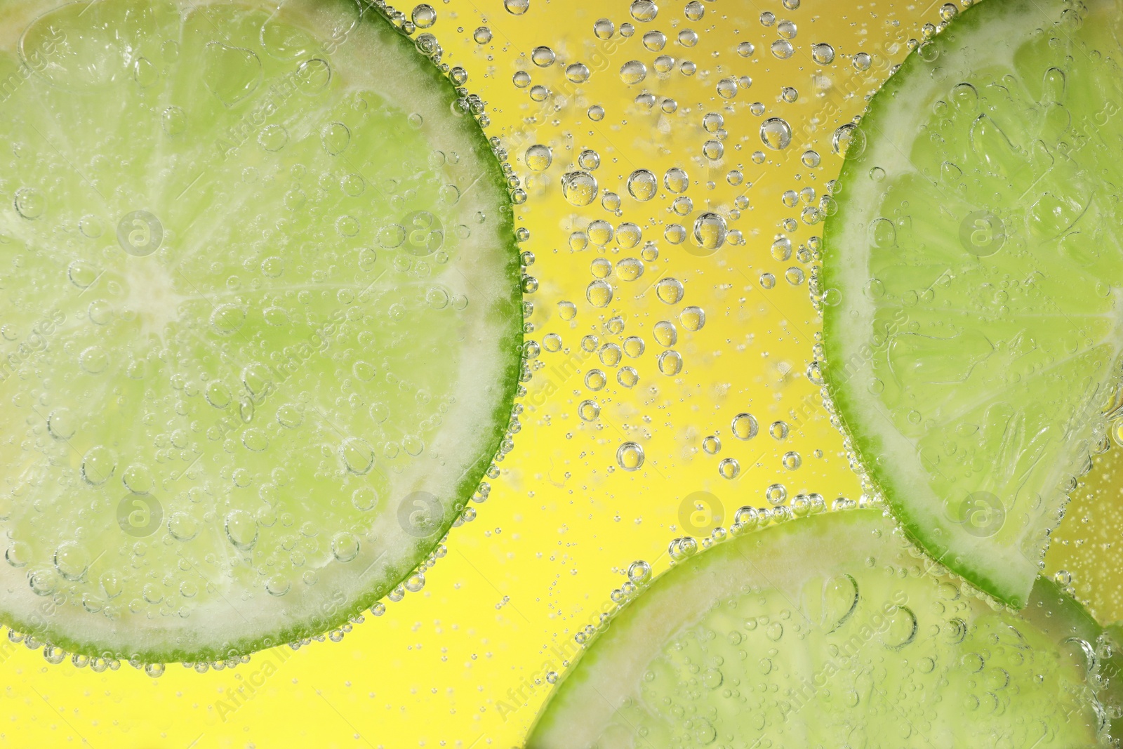 Photo of Juicy lime slices in soda water against yellow background, closeup