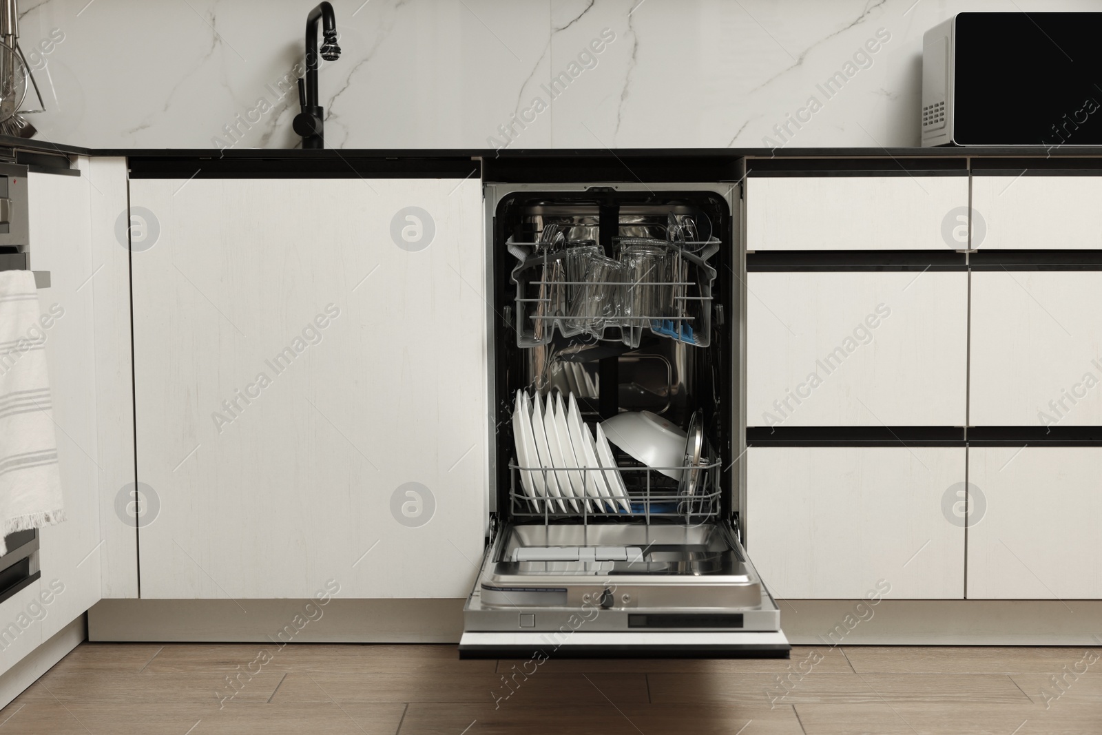 Photo of Open modern dishwasher with different tableware in kitchen