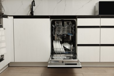 Photo of Open modern dishwasher with different tableware in kitchen