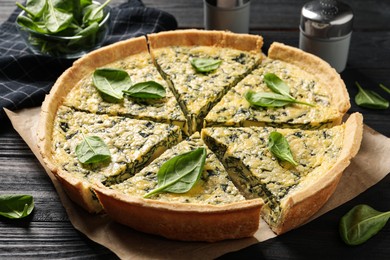 Photo of Sliced delicious homemade spinach pie on black wooden table
