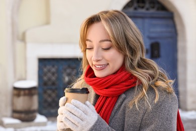 Portrait of smiling woman with paper cup of coffee on city street in winter