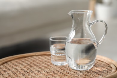 Photo of Jug and glass with clear water on wicker surface against blurred background, closeup. Space for text