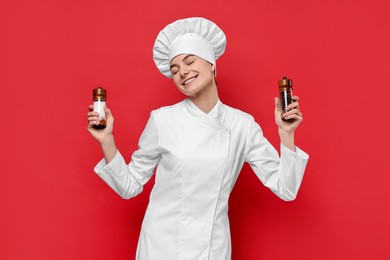 Photo of Professional chef holding salt and pepper shakers on red background
