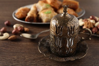 Photo of Beautiful cup holder, nuts and baklava dessert on wooden table, closeup