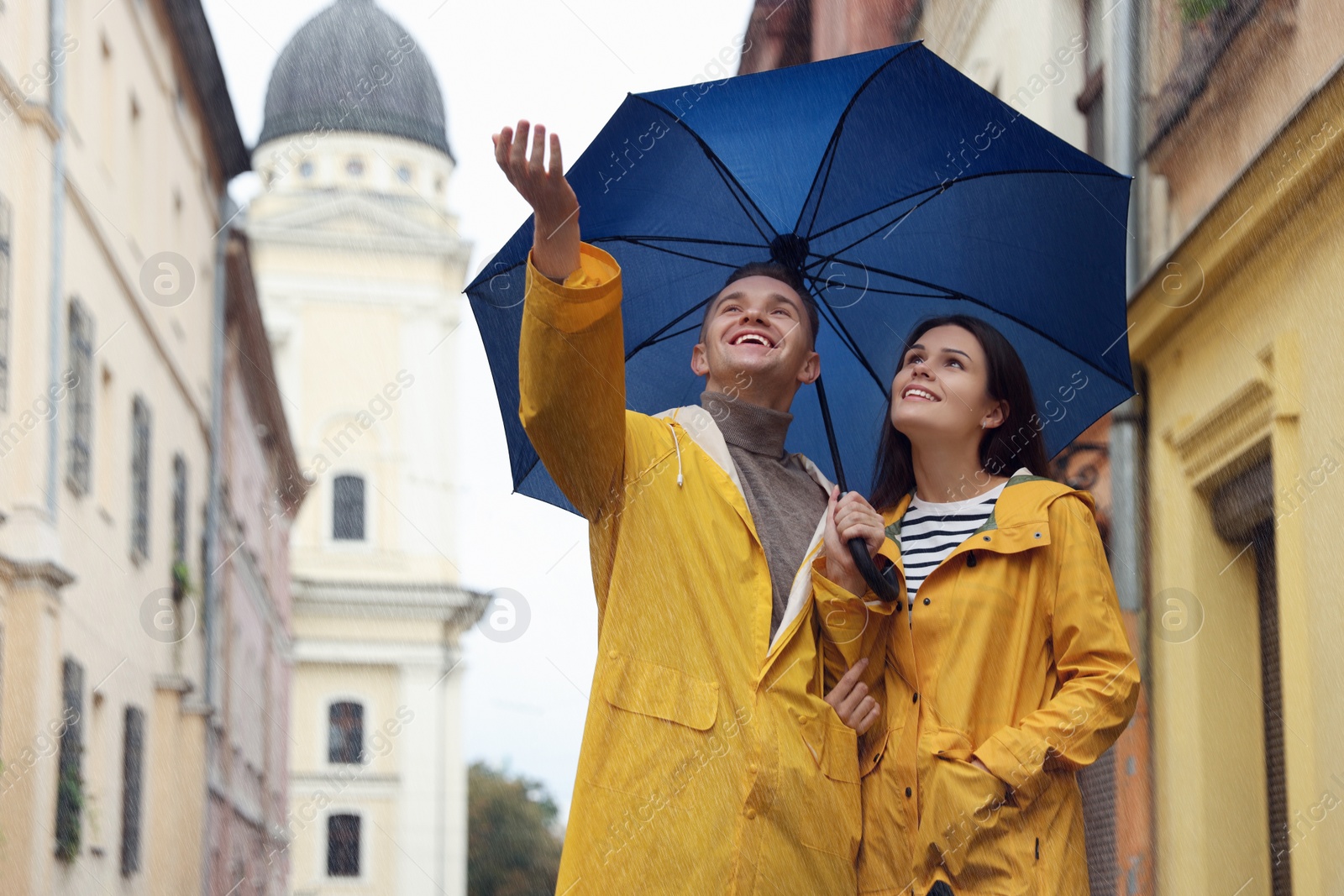 Photo of Lovely young couple with umbrella walking under rain on city street