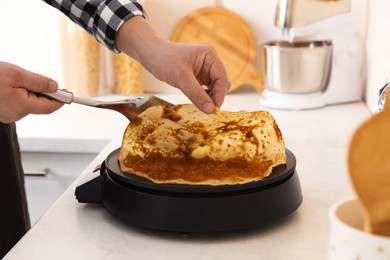 Man cooking delicious crepe with jam on electric pancake maker in kitchen, closeup