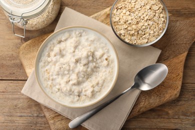 Photo of Tasty boiled oatmeal in bowl, flakes and spoon on wooden table, flat lay