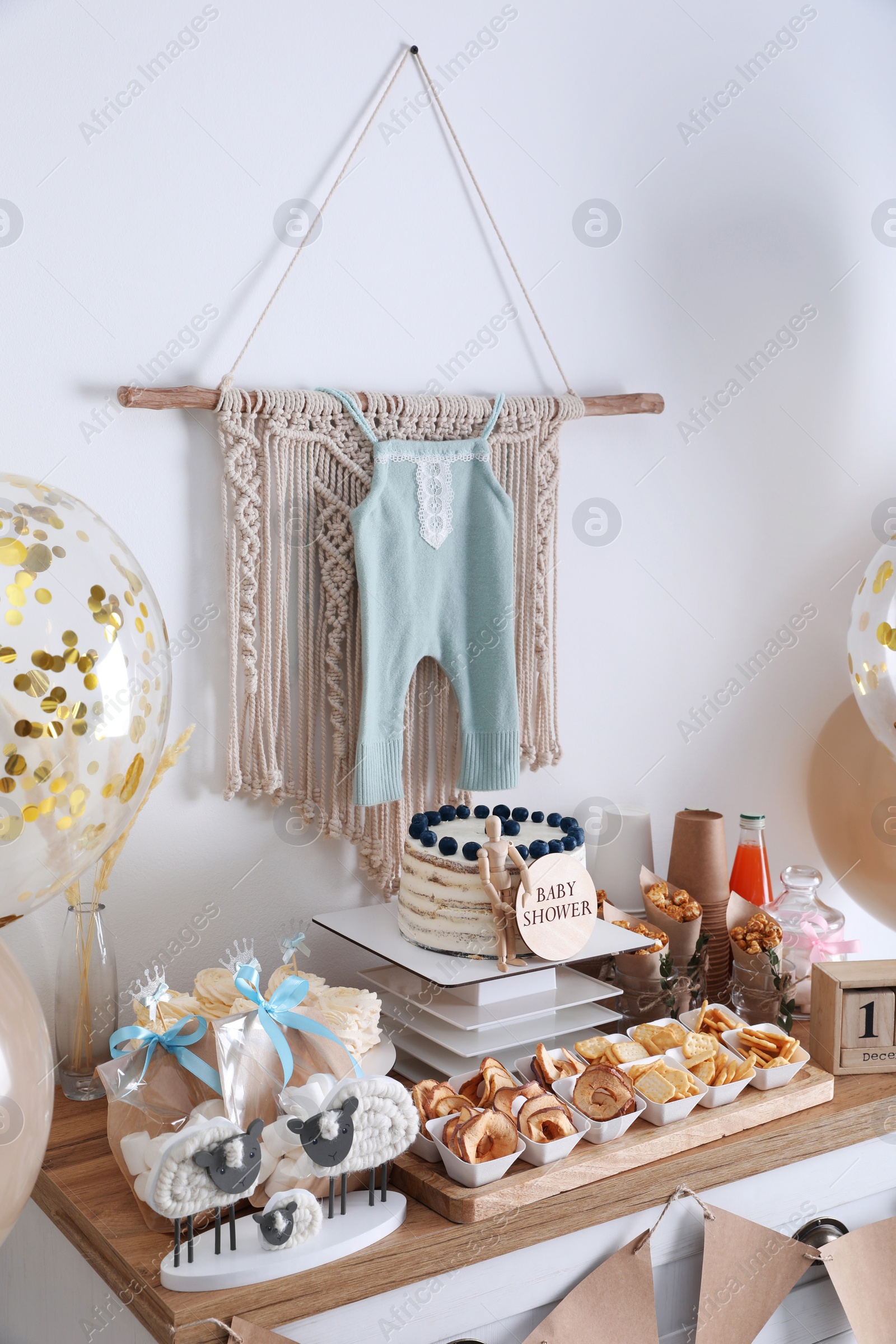 Photo of Baby shower party. Different delicious treats on white wooden chest of drawers and decor near light wall