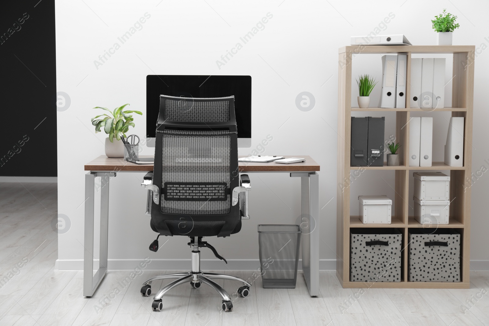 Photo of Cozy workspace with computer on desk, chair and bookcase near white wall at home