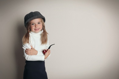 Cute little child in hat with smoking pipe playing detective on beige background, space for text