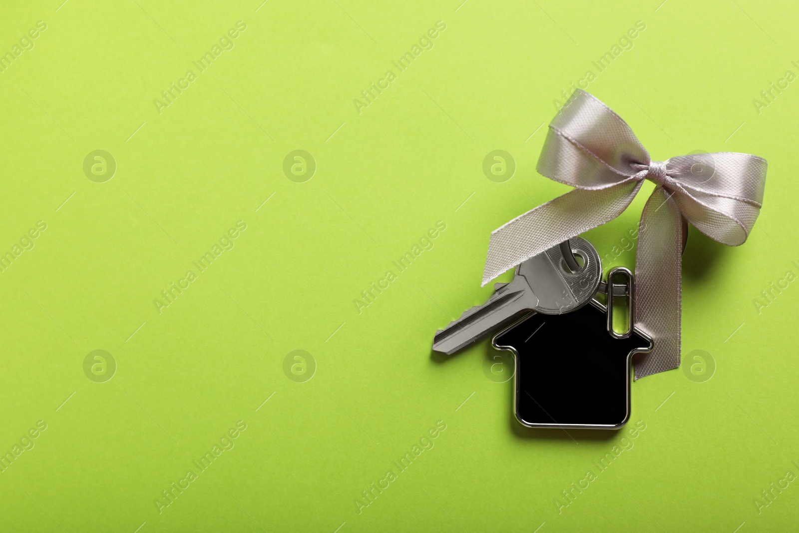 Photo of Key with trinket in shape of house and bow on light green background, top view. Space for text. Housewarming party