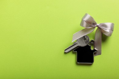 Photo of Key with trinket in shape of house and bow on light green background, top view. Space for text. Housewarming party