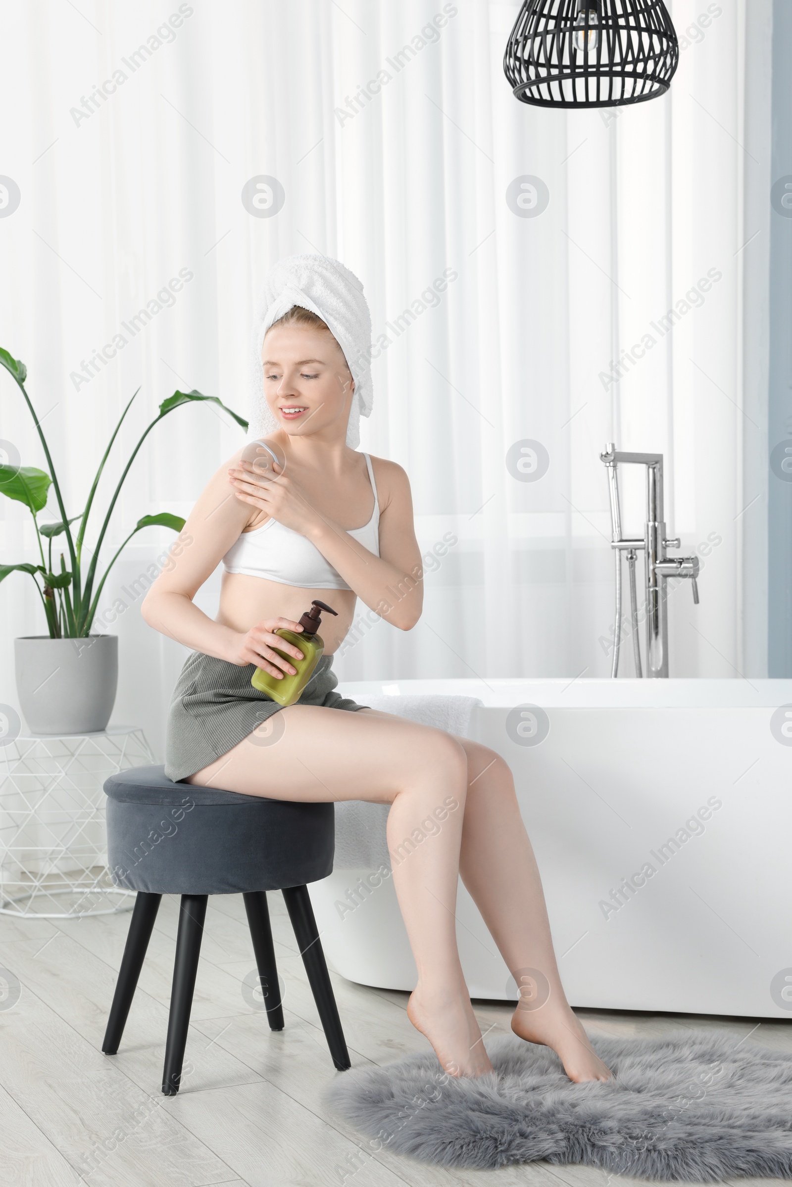 Photo of Beautiful young woman applying oil onto shoulder in bathroom