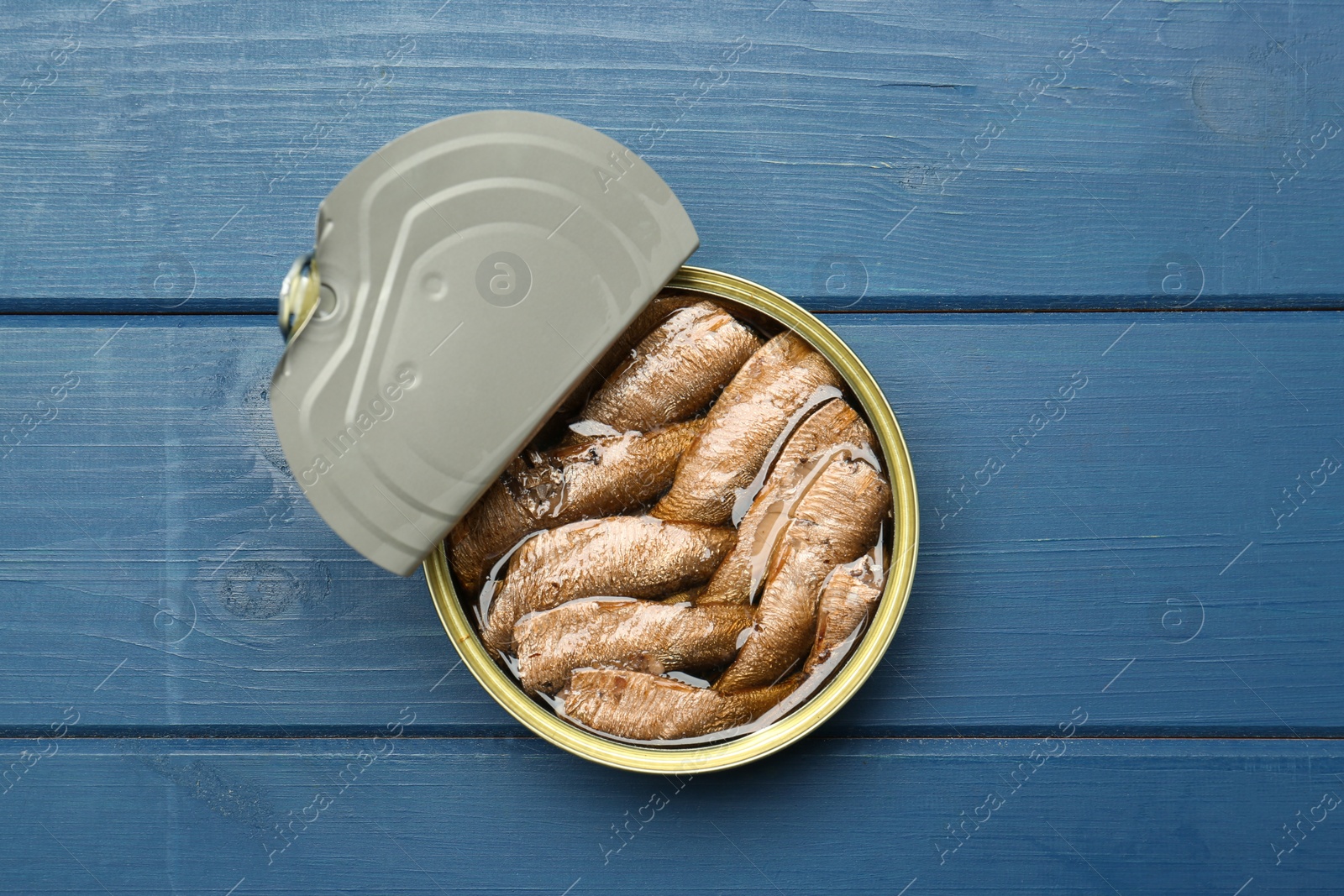 Photo of Open tin can of sprats on blue wooden table, top view