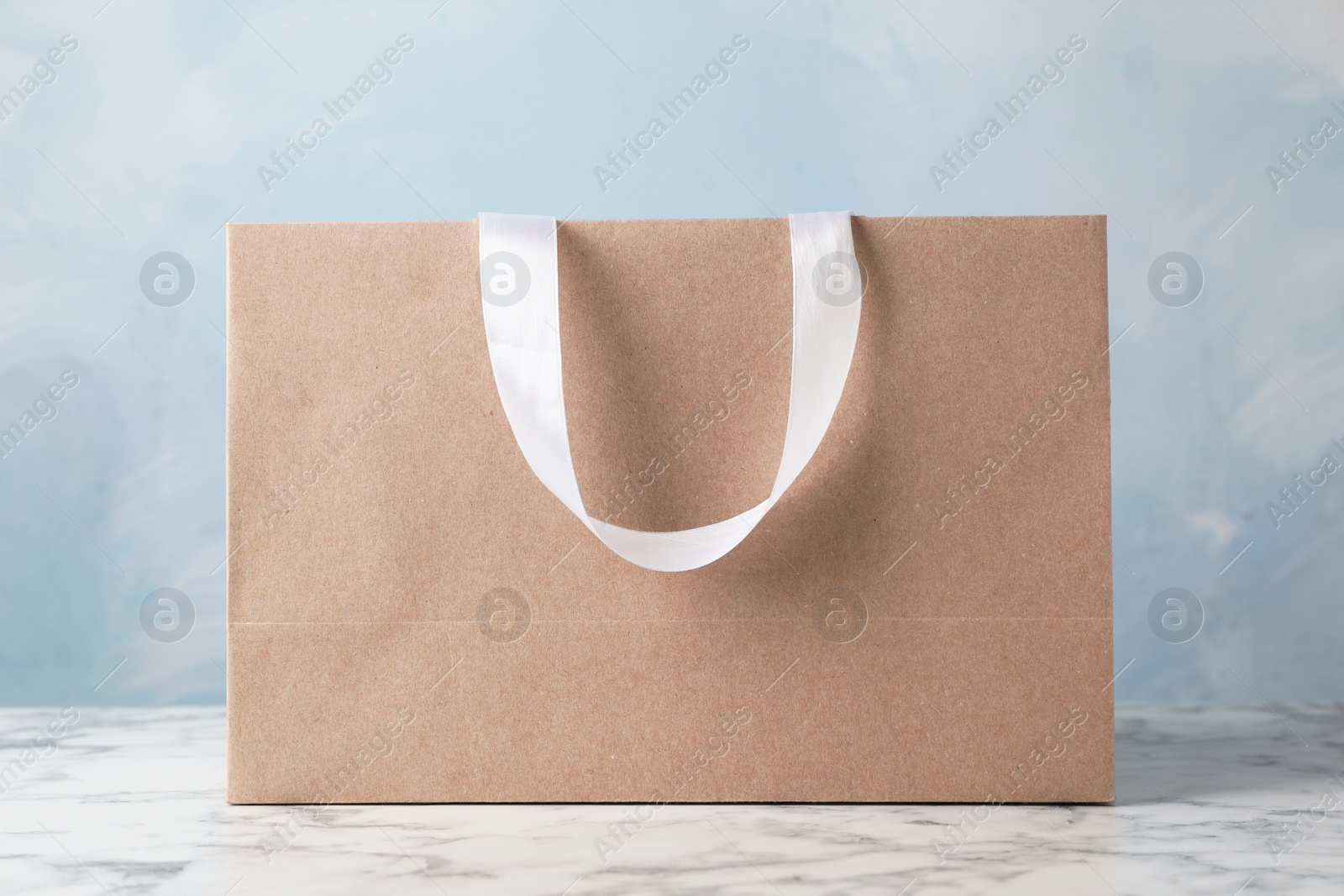 Photo of Paper shopping bag with ribbon handles on table against color background. Mockup for design